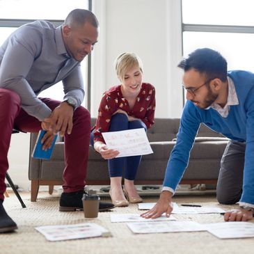 Three colleagues collaborating on a project, reviewing papers on the floor.