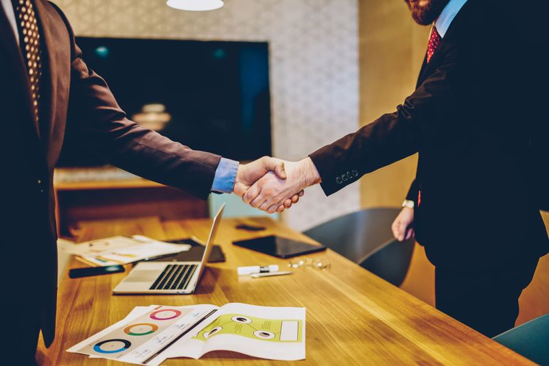 Cropped image of men in suits shaking hands making deal of sponsorship in business corporation, male entrepreneurs agree in partnership cooperation and contract during formal meeting in office
