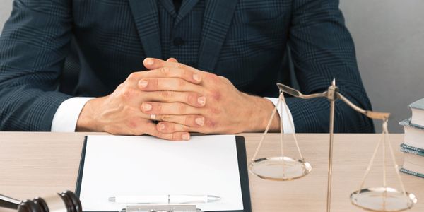 A person in a suit with folded hands at a desk with legal items.