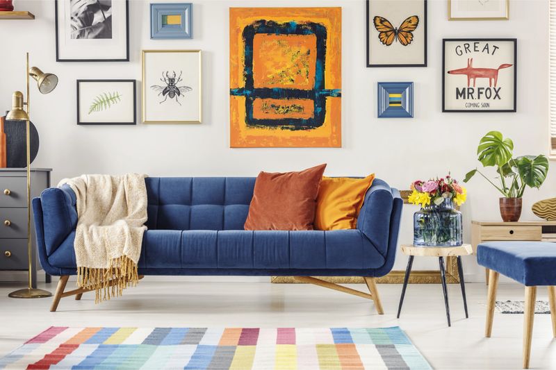 Painting above navy blue couch in artistic living room interior with colorful rug. Real photo