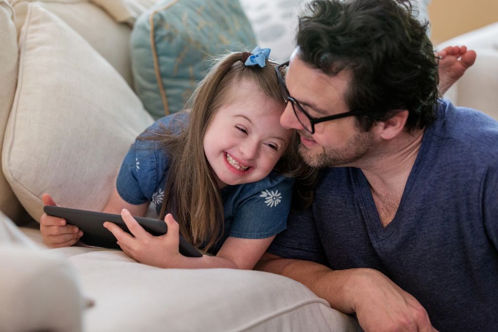 A joyful father and daughter share a loving moment on the couch.