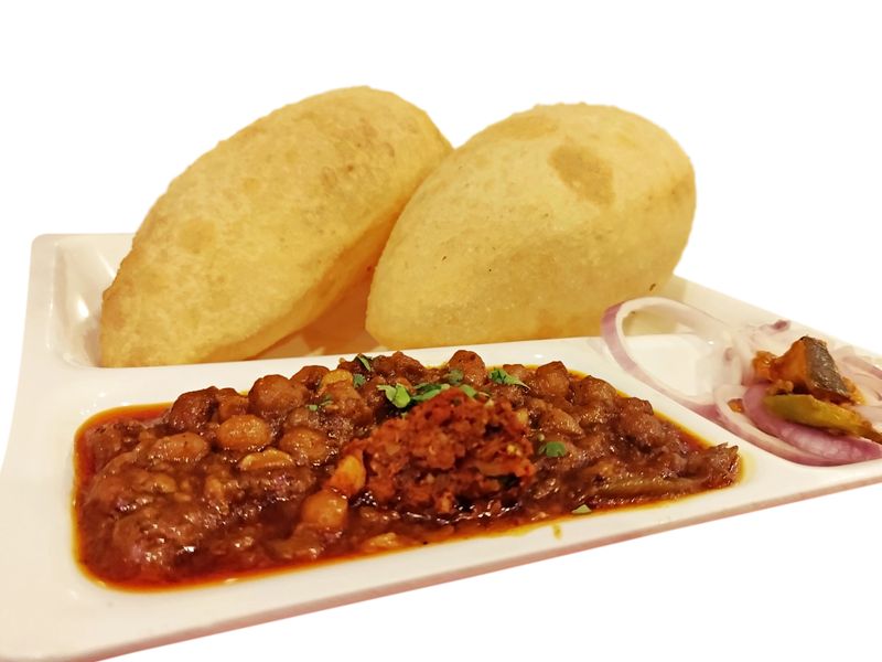 Popular north Indian Punjabi breakfast snack Chhole Bhature. Over white. Mouth watering plating in a white partition plate. Onion rings and pickle on the sides. Eaten as main course.