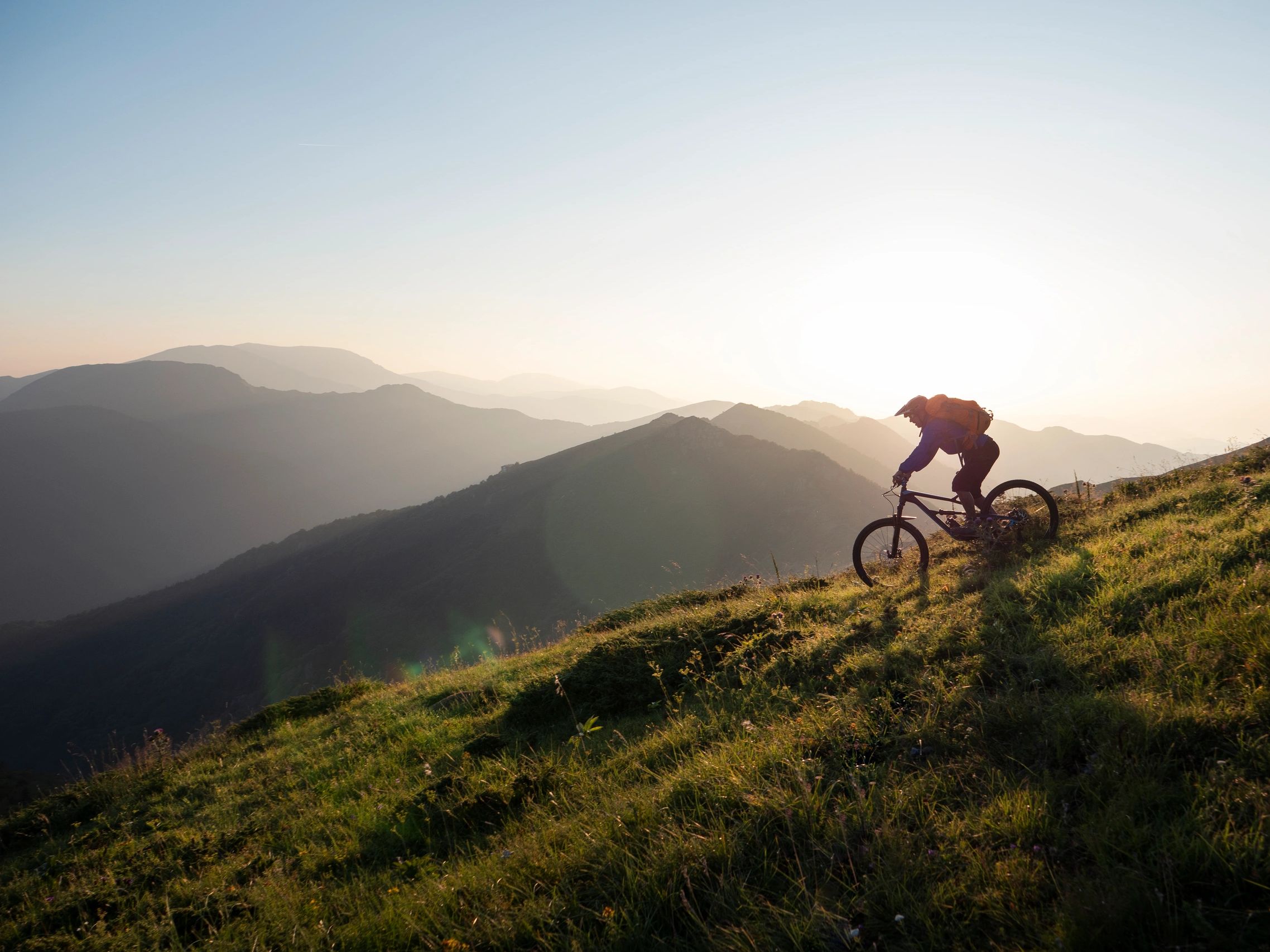 Mountain biker riding downhill at sunrise with misty hills in the background.