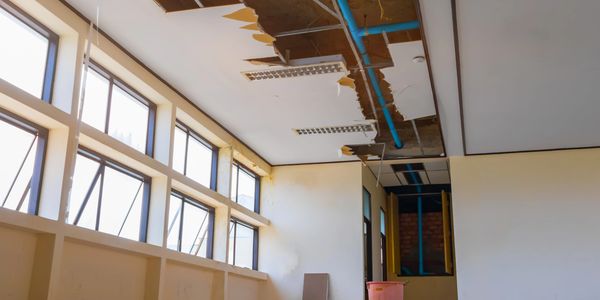 Room with damaged ceiling and exposed pipes.