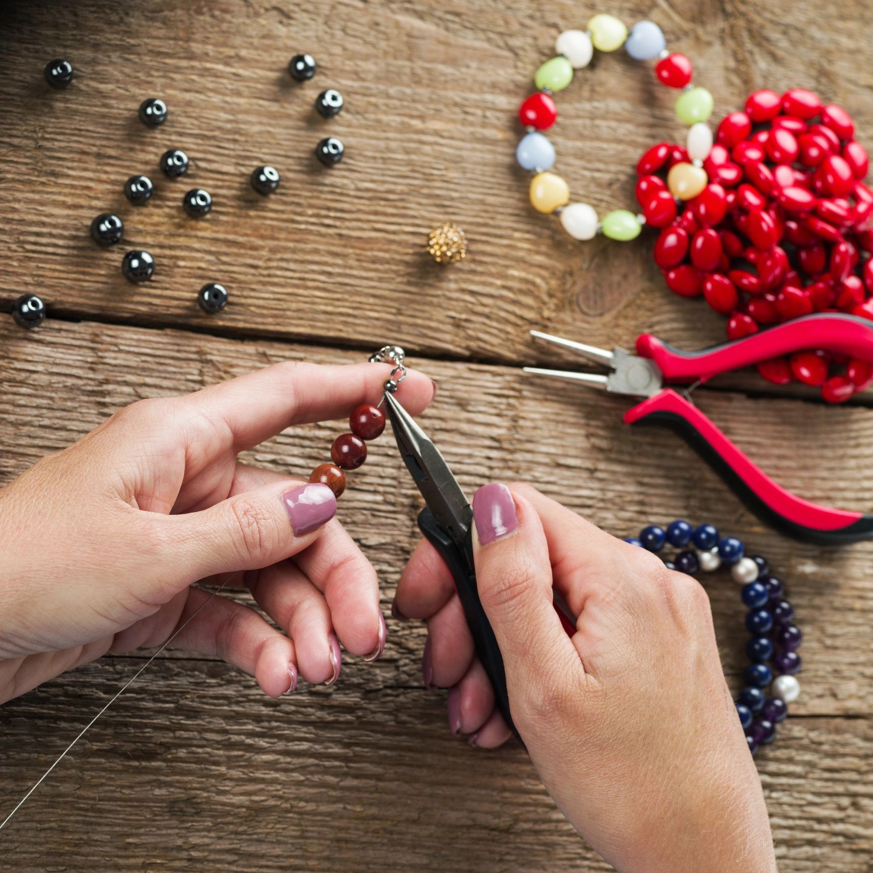 Hands crafting a beaded bracelet with pliers and colorful beads.