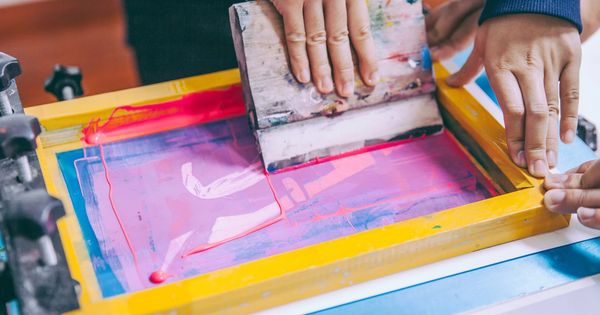 Hands screen printing pink ink onto a surface using a yellow frame.