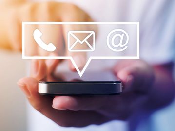 Hand holding smartphone with communication icons floating above.