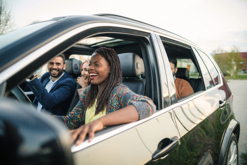 Happy young friends going on a road trip by a car.