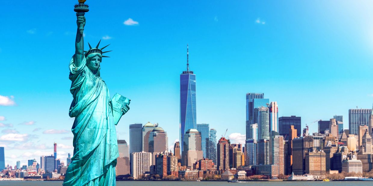 Statue of Liberty with Manhattan skyline in bright daylight.