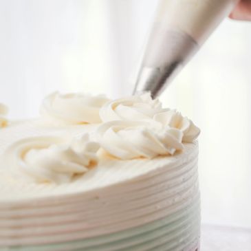 Piping white rose decorations on a cake.