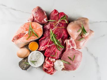 Variety of raw meats and ingredients on marble surface.