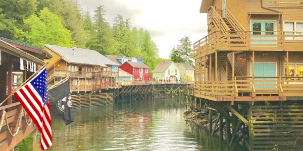 Colorful waterfront buildings on stilts with American flags in a serene setting.