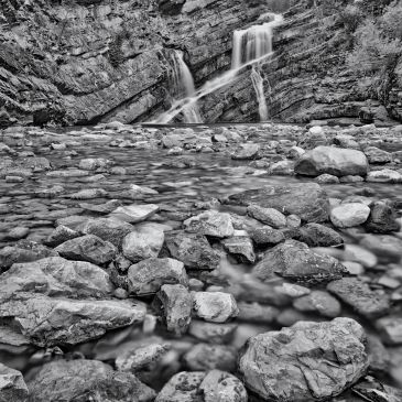 Black and white photo of waterfall over rocks.