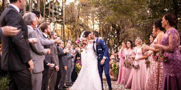 Bride and groom kissing surrounded by wedding party and guests throwing petals.