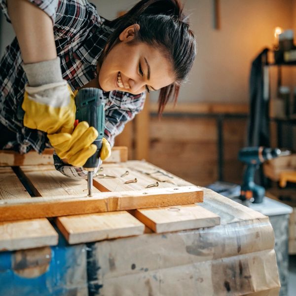 Woman smiling while using a drill on wood.