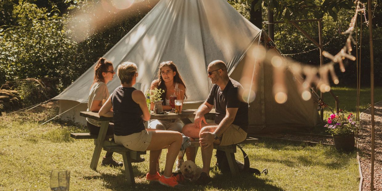 Four people enjoying drinks at a picnic table near a tent.