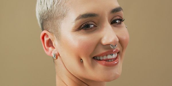 Smiling person with short blonde hair and facial piercings.