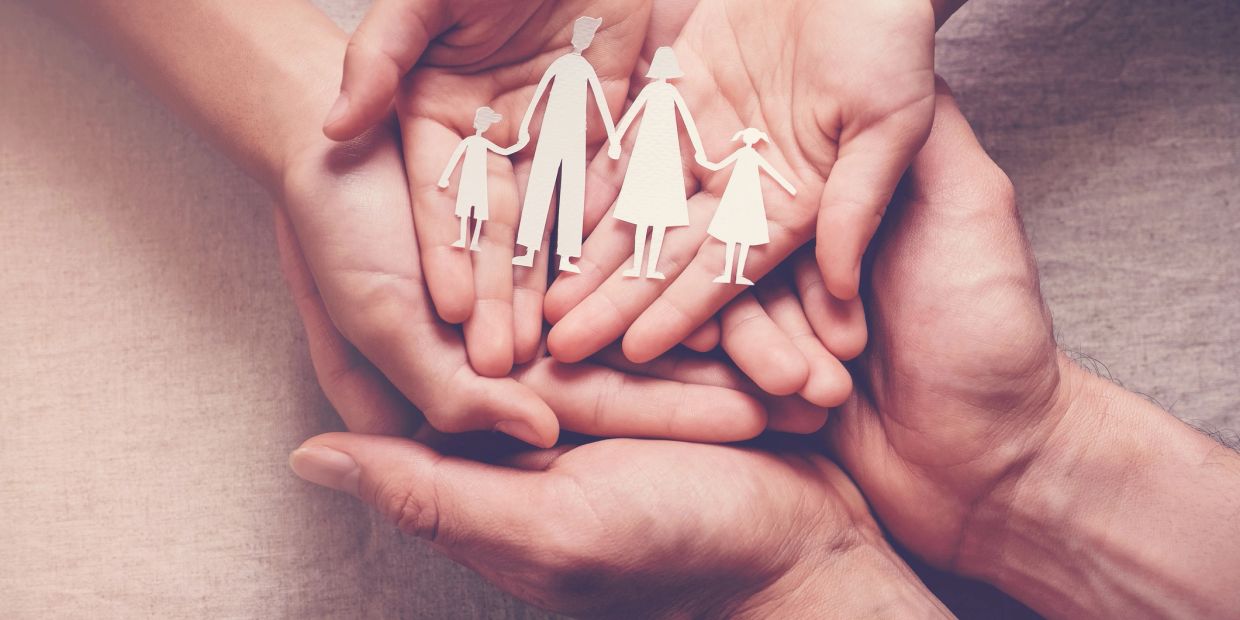 Hands holding paper cutout of a family.