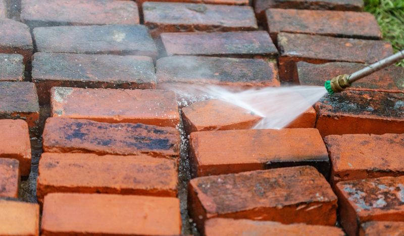 Close up image of reclaimed bricks from a fallen chimney being power-washed to be reused for a new patio.