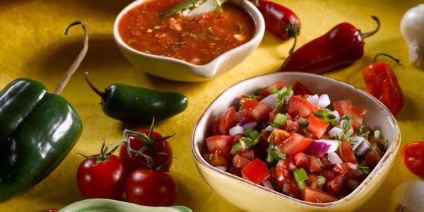 Fresh salsa and ingredients including tomatoes and peppers on a yellow surface.