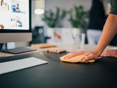 Person cleaning a desk with a yellow cloth near a computer keyboard.