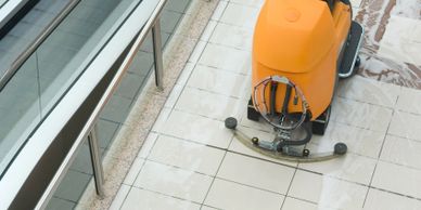 An orange floor cleaning machine on tiled floor near glass panels.