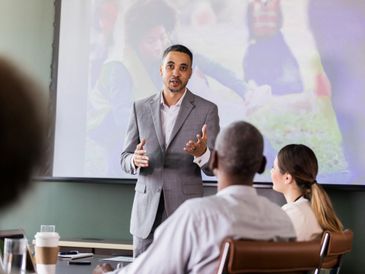 A man in a suit presenting to an attentive audience in a conference room.