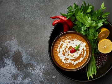 A bowl of creamy lentil soup garnished with chili and cream, surrounded by fresh herbs, lemon, and chili peppers.