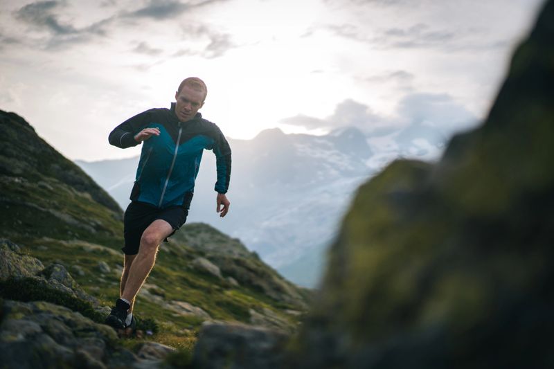 He is on a high mountain path with dramatic sky and clouds behind