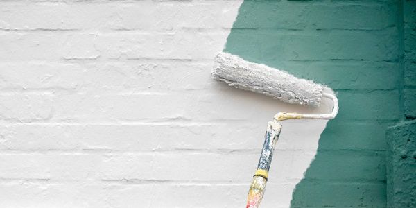 A roller painting a green wall white.