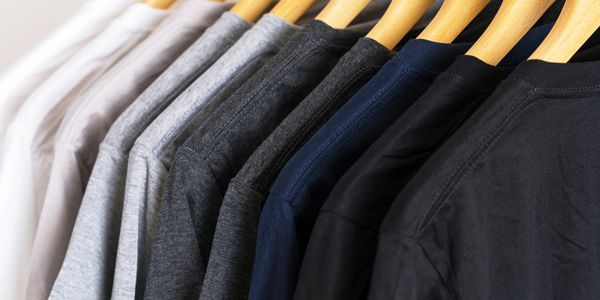 A row of plain t-shirts in neutral colors on wooden hangers.