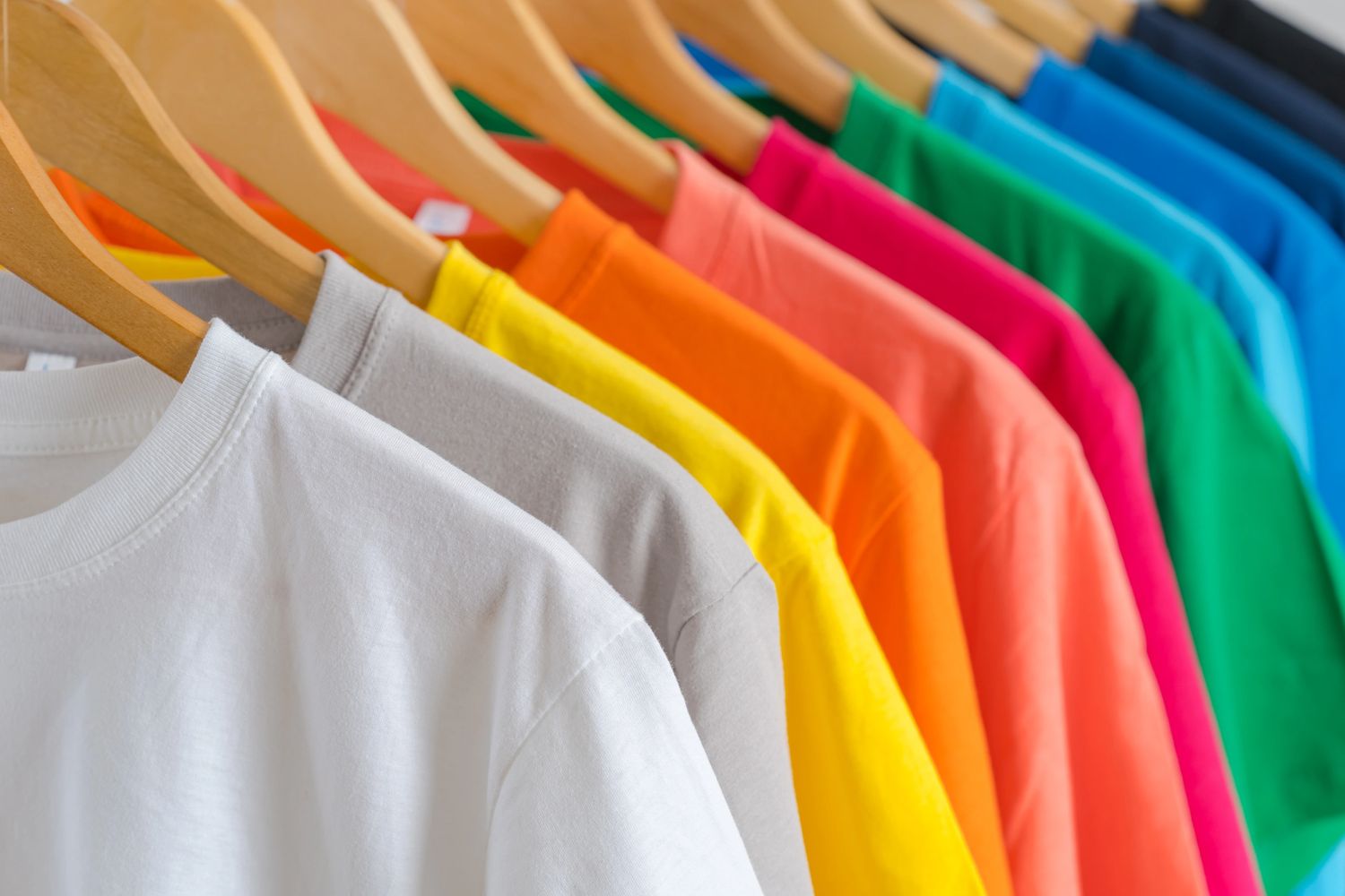 Colorful t-shirts neatly hung on wooden hangers in a row.