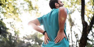 Adult standing outdoors with hands resting on their lower back suggesting discomfort.