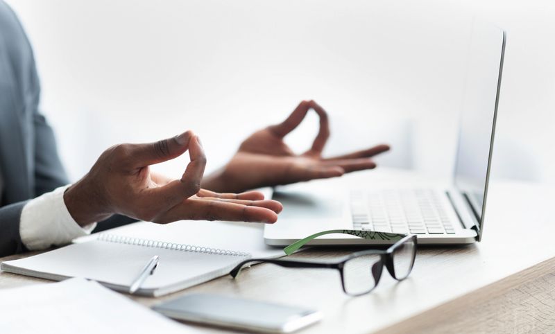 Closeup of black Businessman Meditating In Office, Practicing Yoga At Work, Trying To Handle Stress About Deadline. Panorama with free space