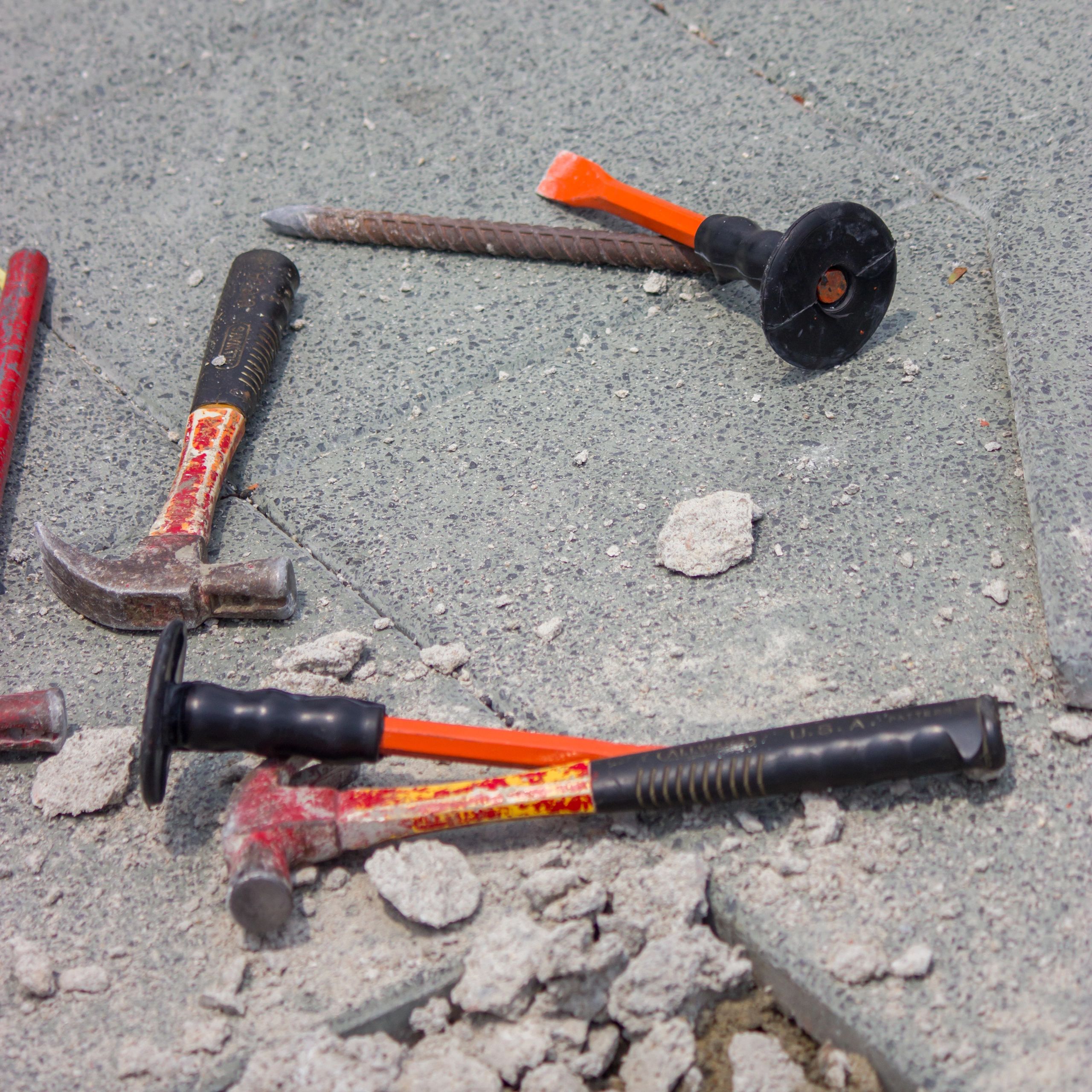 Construction tools, including hammers and chisels, lying on a concrete surface.