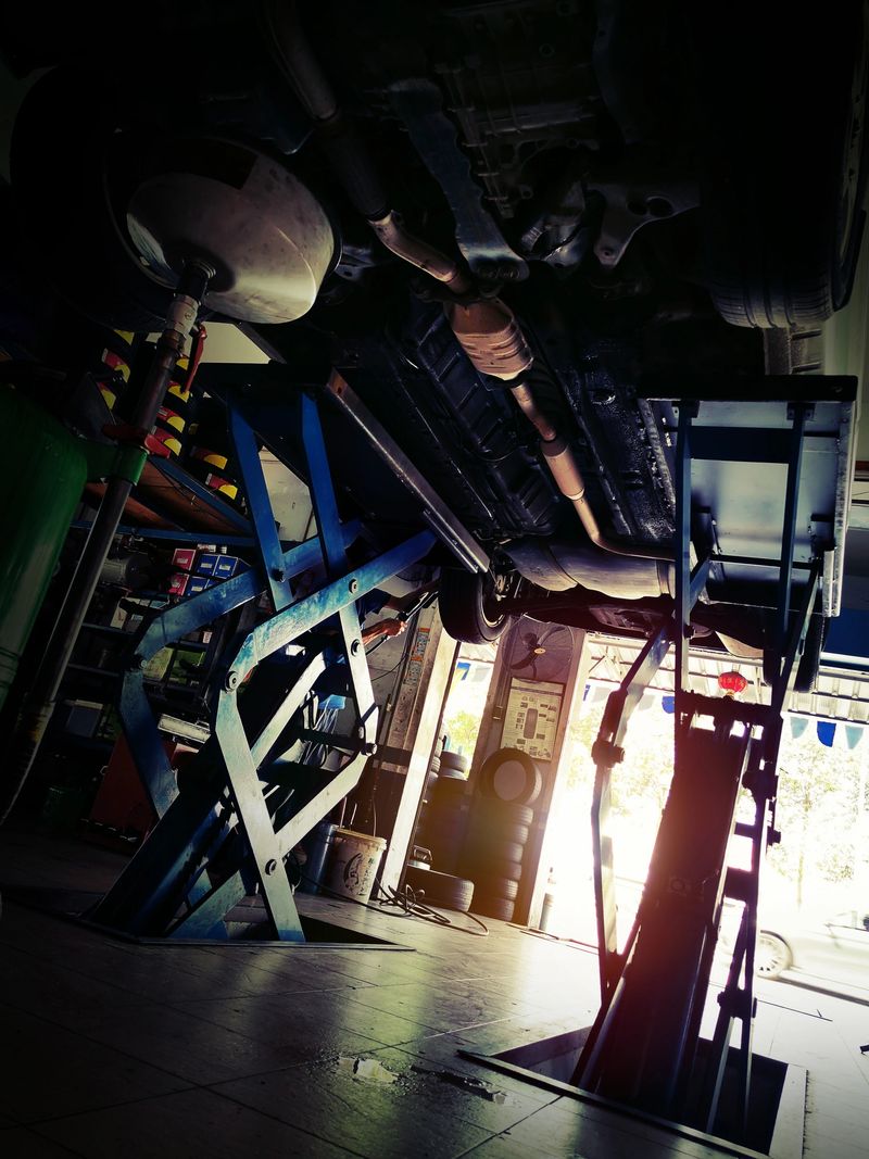 Car service, repair & maintenance. Professional car mechanic man working under lifted car in auto repair service.