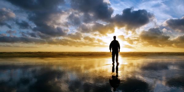 Silhouette of a person standing on a reflective beach during sunset.