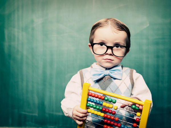 Young boy with glasses holding an abacus in front of a chalkboard.