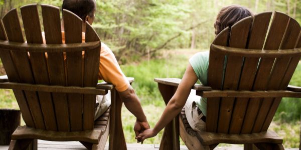 Couple holding hands sitting on wooden rocking chairs outdoors.
