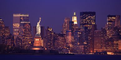 Statue of Liberty illuminated against the New York City skyline at dusk.