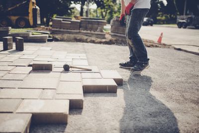 Professional groundworker carefully laying paving slabs on a patio area on a warm, sunny day.
