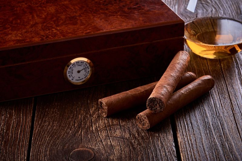 Still life with wooden box for humidification, three cigars and glass of whiskey on old table.
