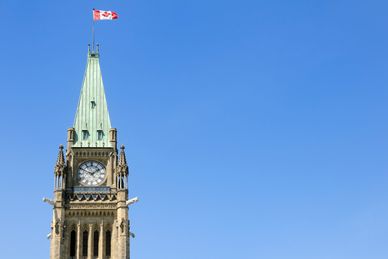 Clock tower with Canadian flag against clear blue sky.