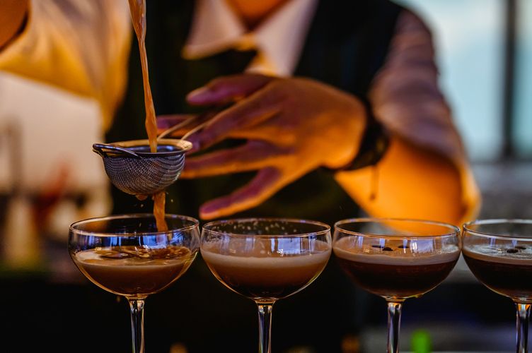 Bartender straining coffee cocktails into glasses with skill.