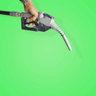 A hand holding a fuel pump nozzle against a green background.