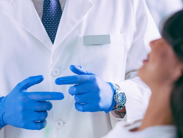 Doctor wearing blue gloves talks to a patient in a white coat.