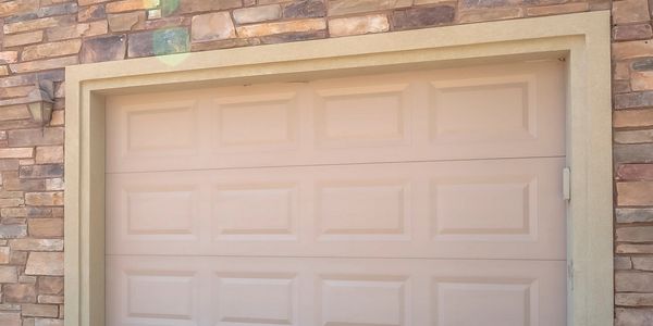Beige garage door with stone wall surrounding it.
