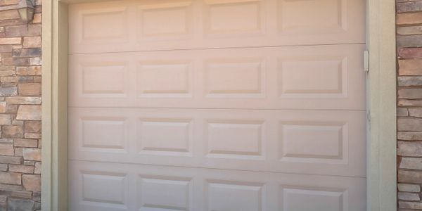 Closed beige garage door set in a stone wall with a concrete driveway.