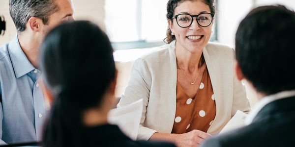 A smiling woman in glasses leads a business meeting with three colleagues.