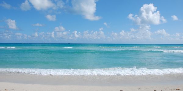 Sunny beach with turquoise waves and fluffy clouds under a blue sky.